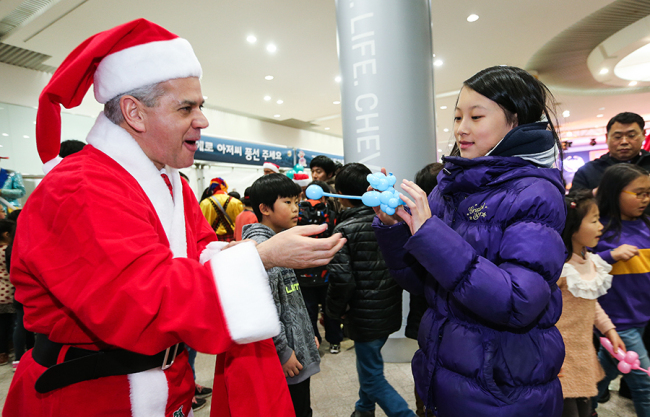 GM Korea CEO Sergio Rocha, dressed as Santa Claus, delivers a puppy-shaped balloon to a girl during a Christmas party for children at the company’s headquarters in Bupyeong, Incheon, Tuesday night. (GM Korea)