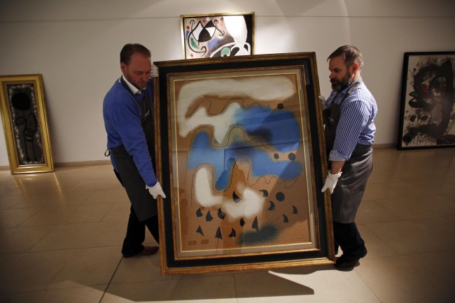 In this Dec. 19 photo, auction house workers carry a painting by Joan Miro in a room with other works of the artist at Christie’s auction house in central London. (AP-Yonhap News)