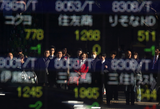 Pedestrians are reflected in a window in front of a stock board outside a securities firm in Tokyo. (Bloomberg)