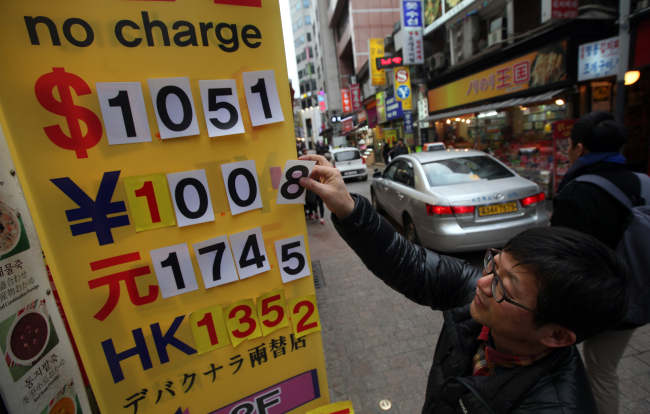 A man alters the exchange rate display in front of a currency exchange broker in Myeong-dong, Seoul, Friday. (Yonhap News)