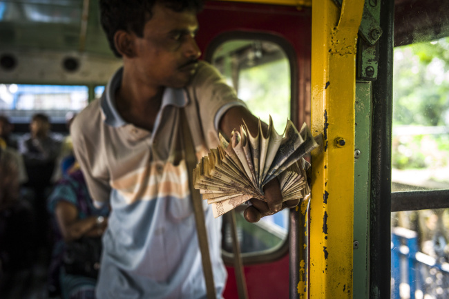 A bus conductor holds a fan of Indian rupee banknotes on a bus in Kolkata, West Bengal, India. (Bloomberg)