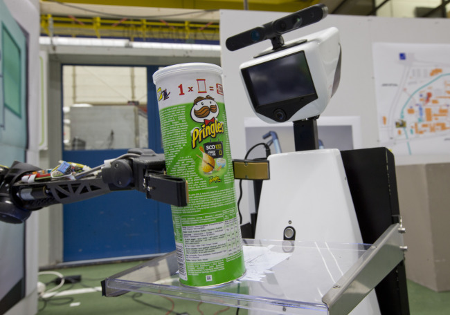 A robotic arm puts a package of Pringles on the serving tray of another robot. (AP-Yonhap News)