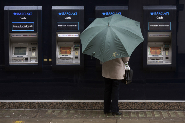 A customer shelters beneath an umbrella as she uses an automated teller machine outside a Barclays Plc bank branch in London. (Bloomberg)