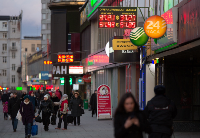 Pedestrians pass illuminated signs advertising foreign exchange rates in Moscow. (Bloomberg)