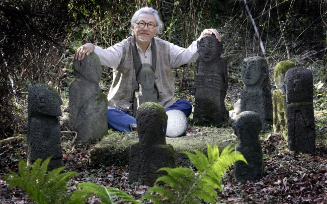 Paek Un-chol, general director of planning, design and installation for Jeju Stone Park, sits with stone statues of young boys that once guarded tombs. (Jeju Stone Park)