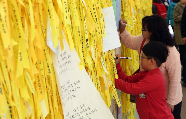 A mother and her son post messages of condolence for victims of the Sewol ferry disaster on Monday. (Yonhap)