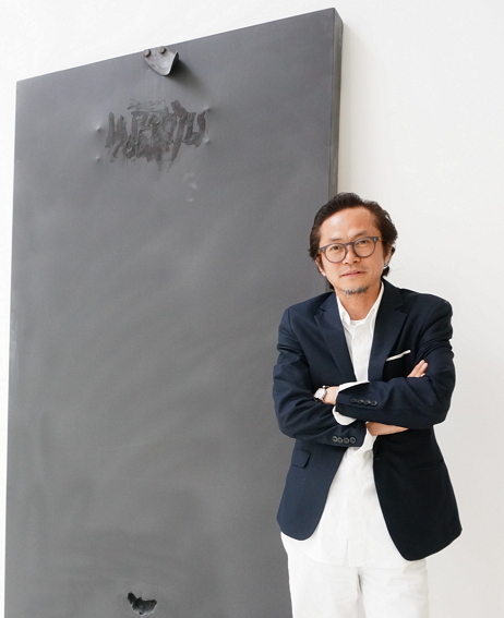Artist Jeong Jai-young poses for a photo in front of one of his paintings at his studio in Busan. (Lee Woo-young/The Korea Herald)