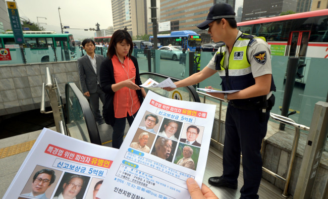 A policeman hands out posters of the wanted Yoo Byung-eon and his eldest son Dae-gyun to passersby in downtown Seoul on Monday. (Kim Myung-sub/The Korea Herald)