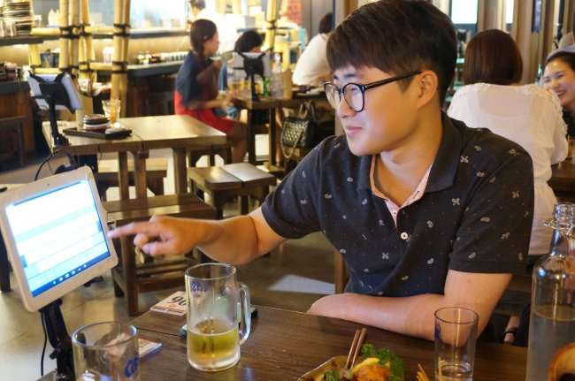 A customer uses a text messaging service at Pocha Factory to join a group of girls at the next table for a drink Monday. (Suk Gee-hyun/ The Korea Herald)