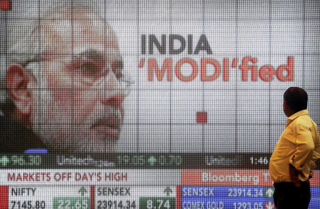 A man looks at a screen showing television coverage of Indian Prime Minister Narendra Modi and the latest figures for the S&P BSE Sensex and the CNX Nifty index at the lobby of the Bombay Stock Exchange in Mumbai. (Bloomberg)