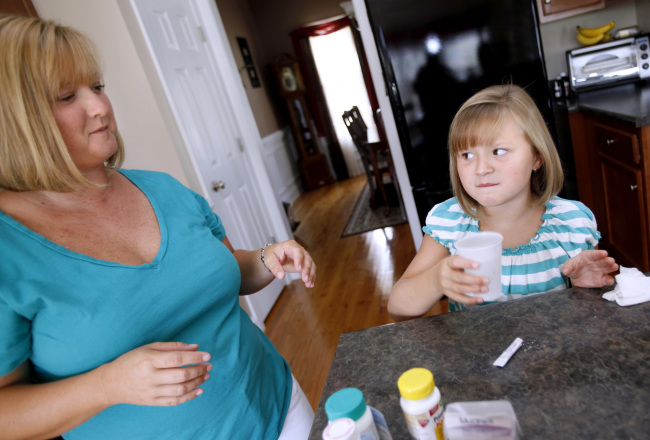 A child who has suffered from a tic disorder takes medication while her mother looks on at their house.(Takaaki Iwabu/Raleigh News & Observer/MCT)