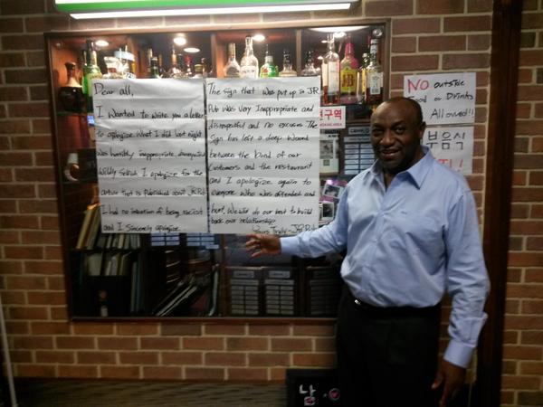 Kenyan Ambassador to South Korea Ngovi Kitau poses on Monday in front of a sign inside JR Pub in Itaewon, Seoul, displaying an apology for a pervious sign that banned Africans from the establishment on Aug. 16. (Philip Iglauer/The Korea Herald)