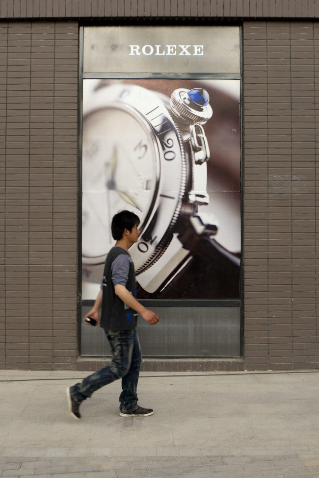 A pedestrian walks past a sign depicting counterfeit Rolex watches in Xi’an, Shaanxi province, China. (Bloomberg)