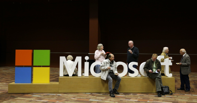 Attendees of Microsoft Corp.’s annual shareholders meeting sit on a Microsoft sign in Bellevue, Washington, last week. (AP-Yonhap)