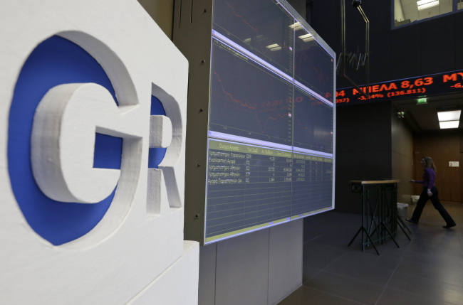 An employee of the Stock Exchange walks by a display board showing losses for Greek shares in Athens on Monday. (AP-Yonhap)