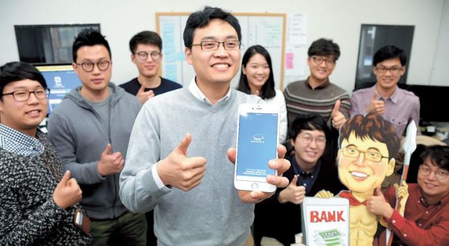 Viva Republica CEO and founder Lee Seung-gun (center) poses with the company’s mobile money transfer app Toss in its office in Seoul. (Park Hyun-koo/The Korea Herald)
