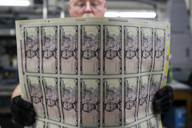 An employee uses a vibrating table to loosen stacks of $5 notes before they are cut into singles at the Bureau of Engraving and Printing in Washington. (Bloomberg)