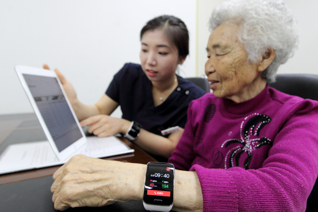 Ha Young-sook (right), an 84-year old resident of Baengnyeongdo Island, checks her heart rate with a smart watch and a tablet PC at the local health center Tuesday. (KT)