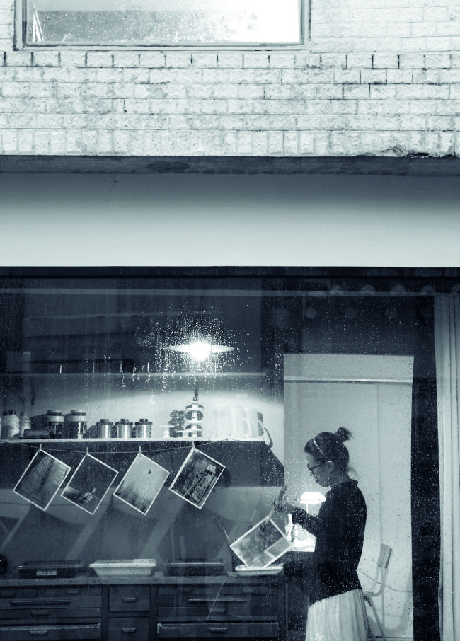 A woman makes a black-and-white print in a dark room. (Mulnamoo Photo Studio)