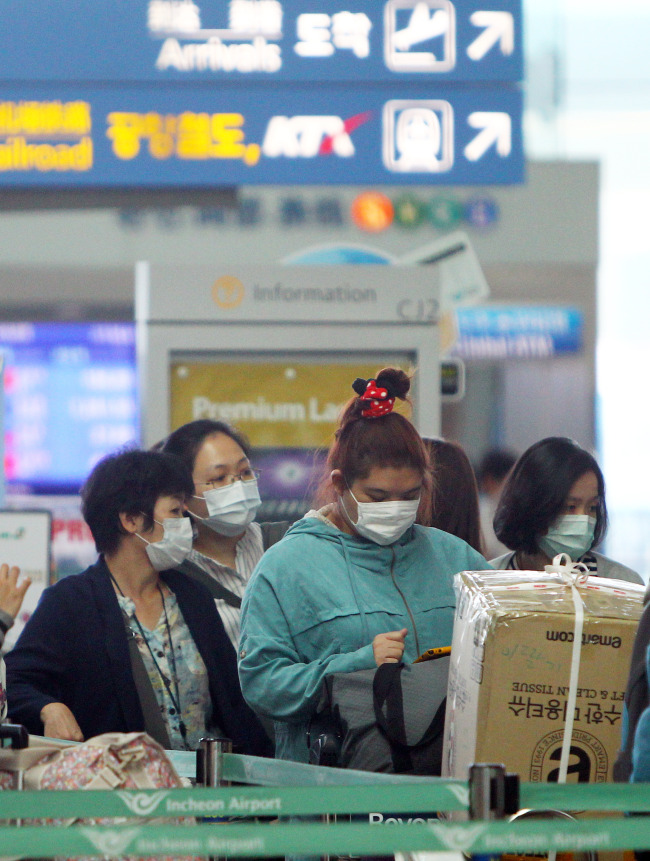 Passengers wearing masks queue to check in at Incheon International Airport in Incheon on Sunday. (Xinhua-Yonhap)