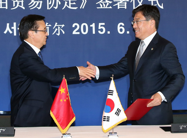 South Korean Trade, Industry and Energy Minister Yoon Sang-jick (right) shakes hands with his Chinese counterpart Gao Hucheng after signing a bilateral free trade agreement in Seoul on Monday. (Yonhap)