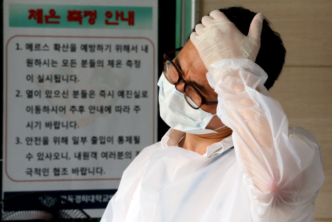 A hospital official in charge of measuring visitors' temperature wipes the sweat off his brow at the entrance of a hospital in Seoul on Wednesday. (Yonhap)
