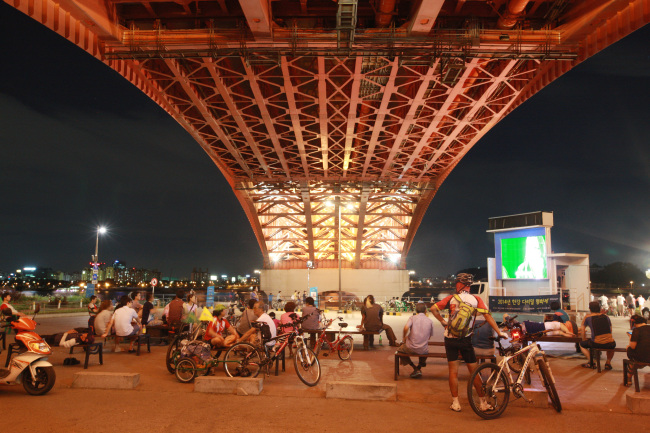 People watch a movie on a screen set up under the Cheongdam Bridge, southern Seoul, as part of summer riverside festival. (Seoul Metropolitan Government)