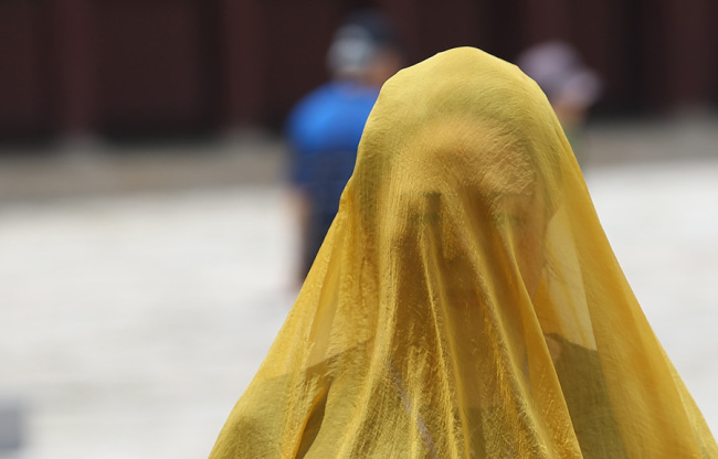 A woman veils her face with a scarf to escape the sun in this July 2015 photo (Yonhap)