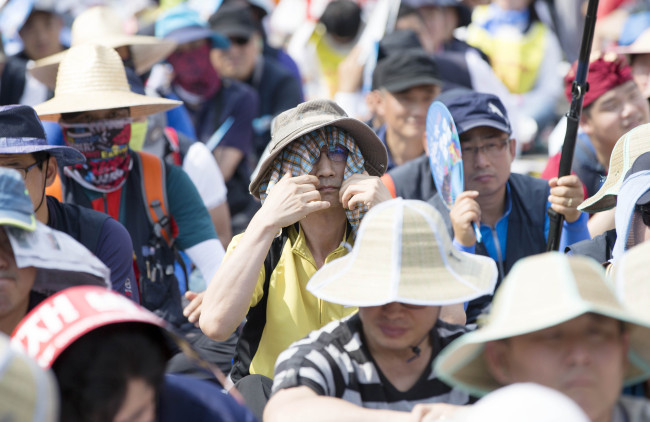 Protesters at Seoul Station Plaza shield their faces from the sun with hats and scarves last month. (Yonhap)