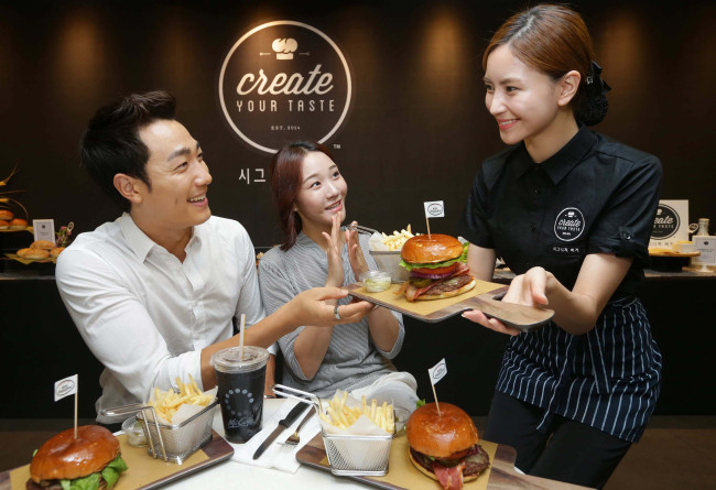 A McDonald’s Korea staff member serves the new “Signature Burger” to customers at its Sinchon store in Seoul, Wednesday. (McDonald’s Korea)