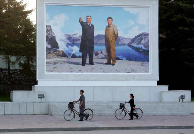 Locals push their bicycles past a large painting depicting North Korean leaders Kim Il-sung (left) and Kim Jong-il in Wonsan, North Korea, Monday. (AP-Yonhap)