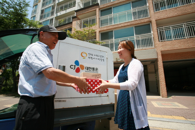 An elderly delivery staff member of CJ Korea Express passes over a parcel to a customer. CJ Korea Express