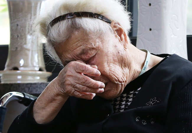 A Korean woman who was forced into sexual slavery during the World War II sheds tears while watching TV news on a summit between Park and Abe on Monday. (Yonhap)