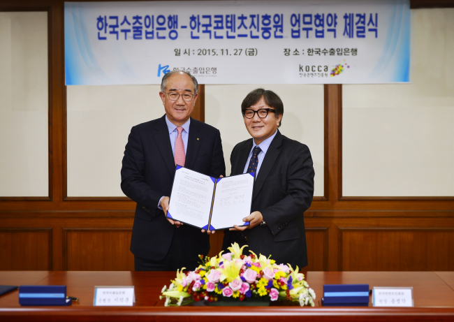 Korea Eximbank president Lee Duk-hoon (left) and KOCCA president Song Sung-gak pose after signing a business cooperation deal in Seoul on Friday. Korea Eximbank