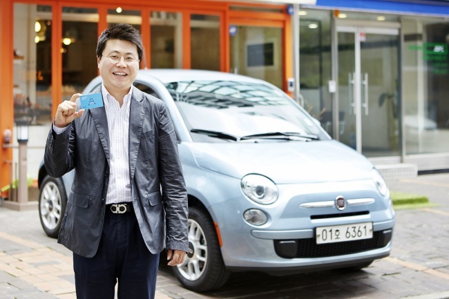 SoCar CEO Kim Ji-mahn poses against the backdrop of the company-owned Fiat 500, a tiny Italian car, while presenting a membership card used for the firm’s car sharing service in Seoul. (SoCar)