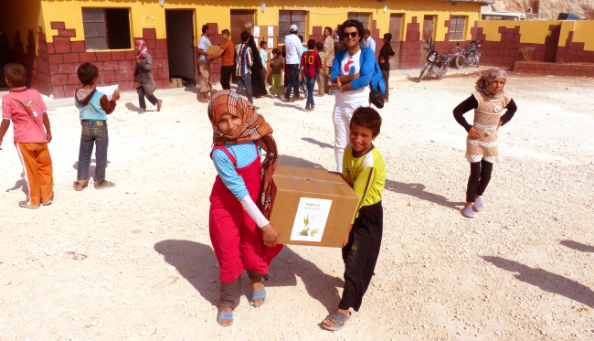 Syrian children carry aid boxes provided by the Help Syria humanitarian organization last year. In the blue shirt is group director Abdul Wahab Almohammad Agha. Help Syria