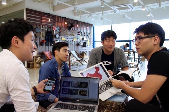 Lee Min-seok (left), co-founder and general director of mobile travel application start-up TNDN, meets with colleagues. (Kakao)