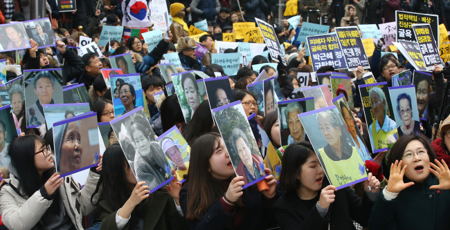 Participants hold up pictures of victims of Japan`s WWII sexual slavery during a weekly rally held near the statue of a girl representing comfort women adjacent to a construction site of the Japanese Embassy building in central Seoul, Wednesday. (Yonhap)