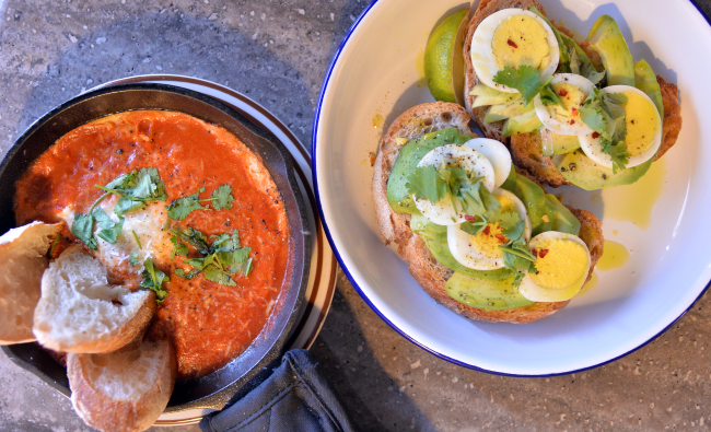 Underyard’s open-faced avocado sandwich (right) is garnished with egg, chili flakes and cilantro and the shakshuka is served up hot in its skillet with slices of baguette (Lee Sang-sub/The Korea Herald)