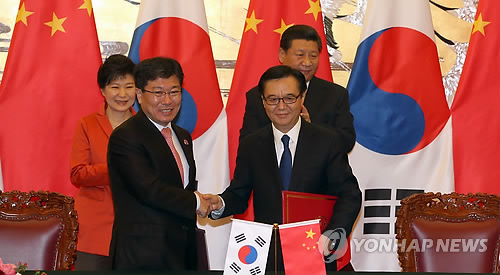 Former Korean Trade Minister Yoon Sang-jick (left) shakes hands with Chinese Commerce Minister Gao Hucheng in November 2014 after signing a free trade agreement. (Yonhap)