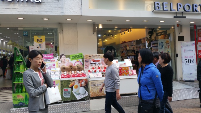 Shoppers in Myeong-dong pass by promotional stands targeting Chinese-speaking tourists. (Won Ho-jung/The Korea Herald)