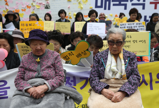 Kim Bok-dong (right) and Kil Won-ok pay silent tribute to Japan’s earthquake victims during the regular Wednesday rally in Seoul on Thursday. (Yonhap)