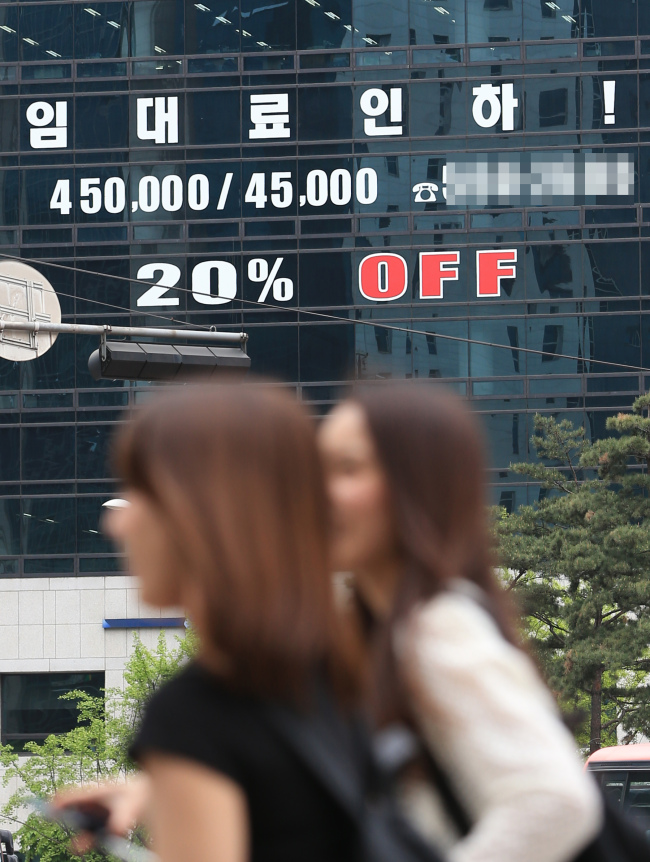 LEASE FEE DISCOUNT -- Two women walk past a building in Gangnam, southern Seoul, which is publicizing a 20 percent discount on the rental fees of offices, on Wednesday. The government said the average vacant ratio of office buildings in Seoul soared to 10.1 percent in the first quarter of this year due to the increased supply of offices and the protracted, sluggish real estate market. (Yonhap)