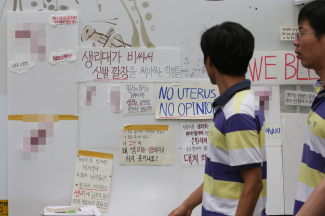 Sanitary pads painted in red and signs that protest the stigma and taboo associated with menstruation are struck in Insa-dong, Seoul, Sunday. The signs say: “Students have to use shoe insoles as alternatives as pads are too expensive” and “Why are pregnancies and deliveries considered sacred while menstruation is not?” (Yonhap)