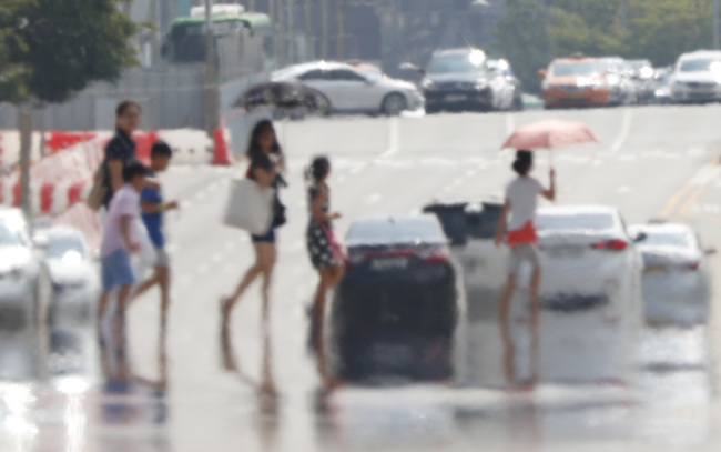 People walk past a pedestrian crossing while the air simmers over a road amid the heat wave that has swept across South Korea. Yonhap
