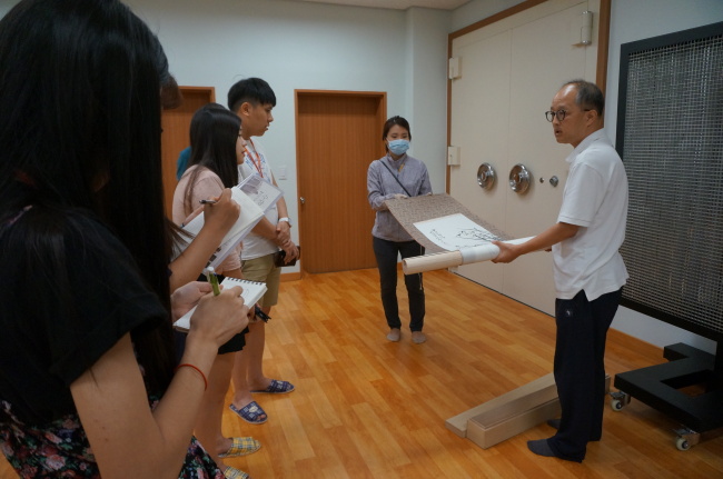 Seo Jun, a curator of the National Palace Museum of Korea, shows how a scroll painting is stored during a museum storage tour on Aug. 10. (Lee Woo-young/The Korea Herald)