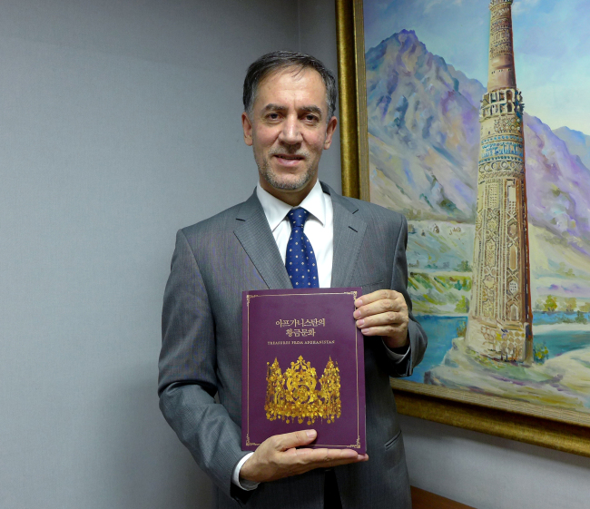 Afghan Ambassador to Korea Mohammad Saleem Sayeb poses with a book published on the occasion of exhibition titled “Treasures from Afghanistan,” which has introduced the country’s ancient relics in Korea for the first time. (Joel / The Korea Herald)
