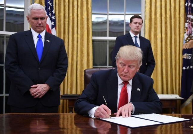 US President Donald Trump signs an executive order as Vice President Mike Pence looks on at the White House in Washington, DC on January 20, 2017. (AFP)