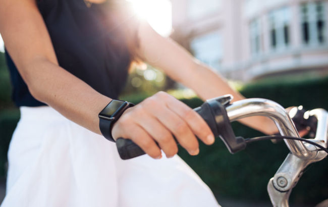 A woman wearing a fitness smartwatch rides a bike (123RF)