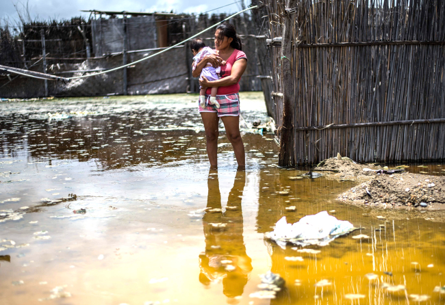 A woman and her baby stand on a flooded street in the northern city of Piura, Peru, on March 25. (AFP-Yonhap)